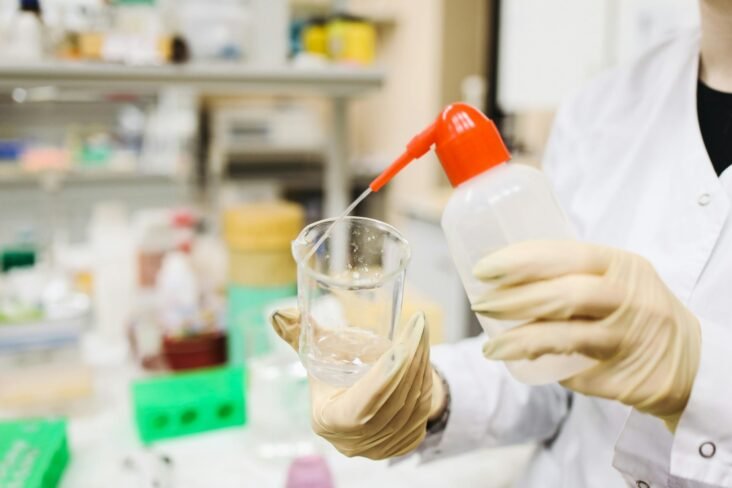 Scientist in gloves pouring liquid into a beaker in a laboratory setting.